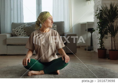Young woman with cancer taking yoga and meditating in her apartment. 101873698