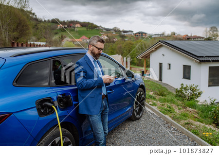 Mature businessman waiting for charging his electric car. Mature businessman waiting for charging his electric car. 101873827
