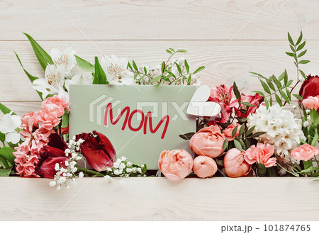 Mom text on card. pink and white garden flowers between white wooden background. Heart and greeting card. Carnations hyacinth roses alstroemeria primrose floral arrangement. 101874765