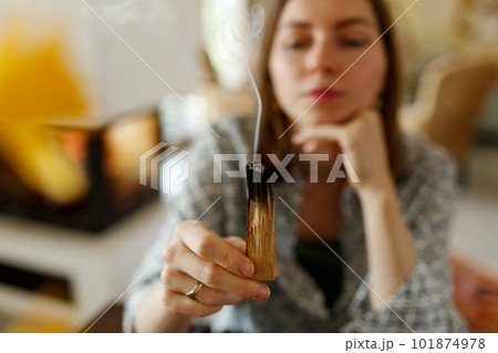 Woman hands burning Palo Santo, before ritual on the table with candles and green plants. Smoke of smudging treats pain and stress, clears negative energy and meditation wooden stick.. Woman hands burning Palo Santo, before ritual on the table with candles and green plants. Smoke of smudging treats pain and stress, clears negative energy and meditation wooden stick.. 101874978