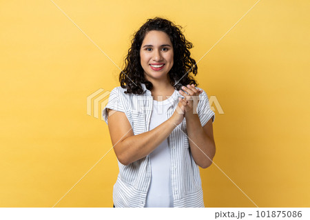 Portrait of delighted satisfied friendly woman with dark wavy hair standing looking at camera with toothy smile, clapping hands. Indoor studio shot isolated on yellow background. Portrait of delighted satisfied friendly woman with dark wavy hair standing looking at camera with toothy smile, clapping hands. Indoor studio shot isolated on yellow background. 101875086