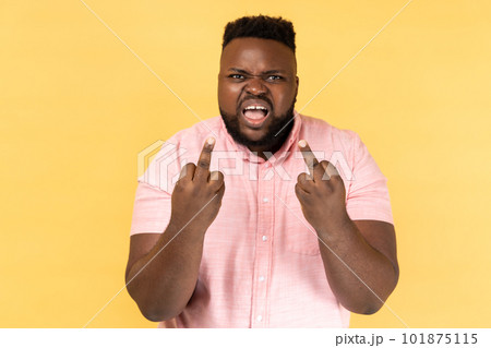 Portrait of impolite aggressive man wearing pink shirt showing middle fingers and asking to get off expressing negativity, disrespectful behaviour. Indoor studio shot isolated on yellow background. 101875115