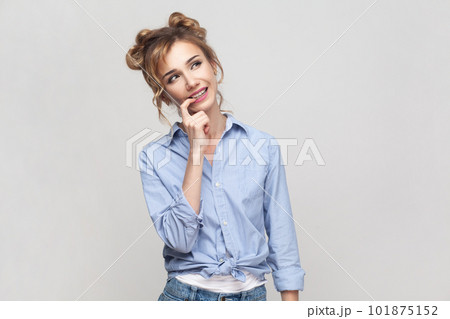 Portrait of pleased dreamy young adult blonde woman looks away with dreamy expression dreams about something, wearing blue shirt. Indoor studio shot isolated on gray background. Portrait of pleased dreamy young adult blonde woman looks away with dreamy expression dreams about something, wearing blue shirt. Indoor studio shot isolated on gray background. 101875152