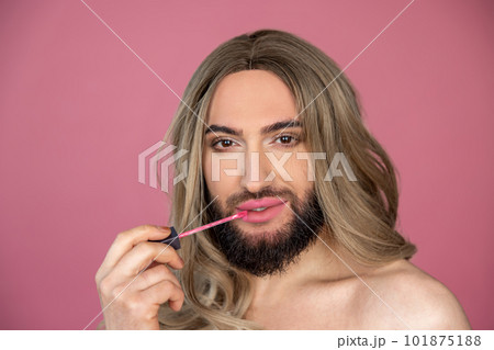 Transgender wearing blonde wig and white dress doing makeup applying lip gloss preparing for party Transgender wearing blonde wig and white dress doing makeup applying lip gloss preparing for party 101875188