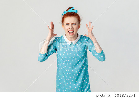 Portrait of angry depressed ginger woman arguing with her husband, screaming with hate and anger, being aggressive, wearing blue dress. Indoor studio shot isolated on gray background. 101875271
