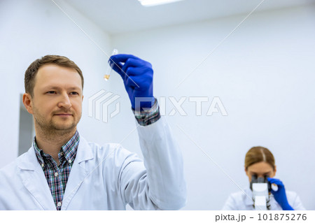 Male scientist analyzes liquid female researcherworking with microscope investigating medical sample Male scientist analyzes liquid female researcherworking with microscope investigating medical sample 101875276