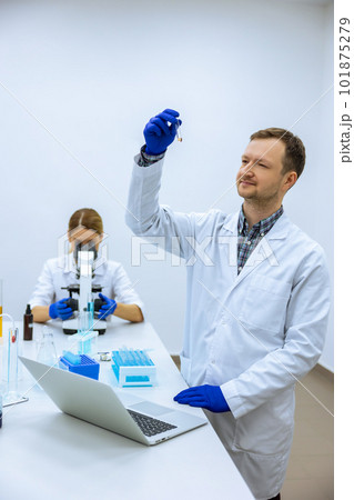 Male scientist analyzes liquid in beaker and types down observations on computer 101875279