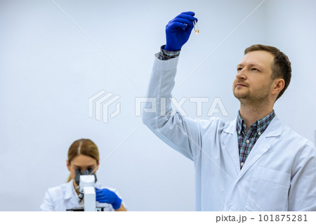 Male scientist analyzes liquid female researcherworking with microscope investigating medical sample 101875281