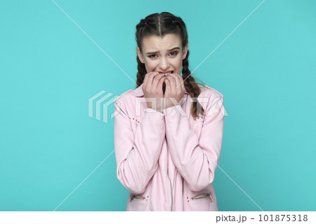 Portrait of nervous stressed teenager girl with braids wearing pink jacket being in deep depression, feels panic attack, biting her fingernails. Indoor studio shot isolated on green background. Portrait of nervous stressed teenager girl with braids wearing pink jacket being in deep depression, feels panic attack, biting her fingernails. Indoor studio shot isolated on green background. 101875318