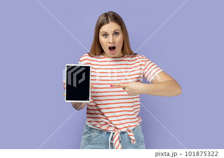 Portrait of amazed shocked surprised blond woman holding pointing at tablet with empty display, mockup screen for your advertisement. Indoor studio shot isolated on purple background. Portrait of amazed shocked surprised blond woman holding pointing at tablet with empty display, mockup screen for your advertisement. Indoor studio shot isolated on purple background. 101875322
