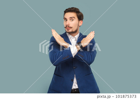 Serious strict man with mustache standing showing x sign, no way gesture, looking at camera with bossy expression, wearing official style suit. Indoor studio shot isolated on light blue background. Serious strict man with mustache standing showing x sign, no way gesture, looking at camera with bossy expression, wearing official style suit. Indoor studio shot isolated on light blue background. 101875373
