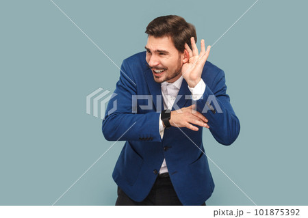 Portrait of handsome man standing with frowning face and hand near ear, trying to listen silent conversation, wearing official style suit. Indoor studio shot isolated on light blue background. Portrait of handsome man standing with frowning face and hand near ear, trying to listen silent conversation, wearing official style suit. Indoor studio shot isolated on light blue background. 101875392