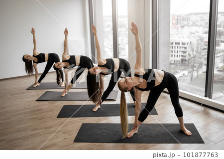 Slim yoginis standing in Triangle pose in studio room 101877763