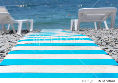 close-up of striped beach path between sun loungers on pebble beach leading to blue sea. summer holiday backdrop. selective focus 101878688