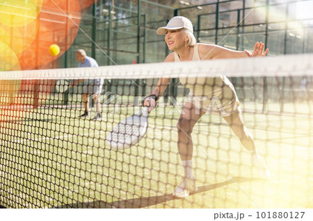 Motivated senior woman playing padel with her teammate in court 101880127