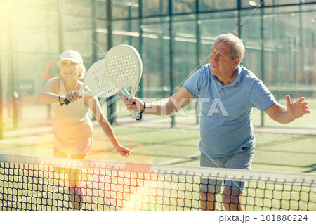 Old man and woman playing Padel Tennis in open-air tennis court Old man and woman playing Padel Tennis in open-air tennis court 101880224