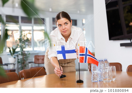 Positive young woman putting flag of Finland on the table with flag of Norway in conference room 101880894