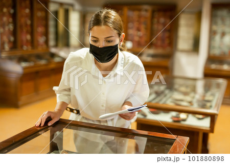 Woman in protective mask exploring artworks in glass case in museum 101880898