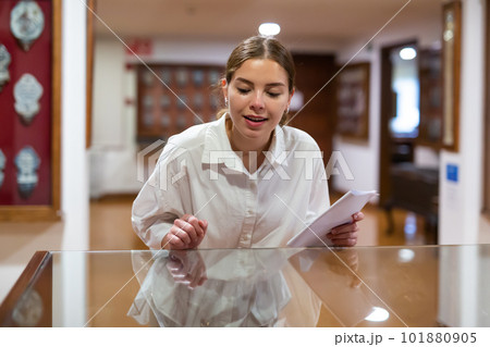 Attentive girl visitor at museum looks at exposition behind glass display case Attentive girl visitor at museum looks at exposition behind glass display case 101880905