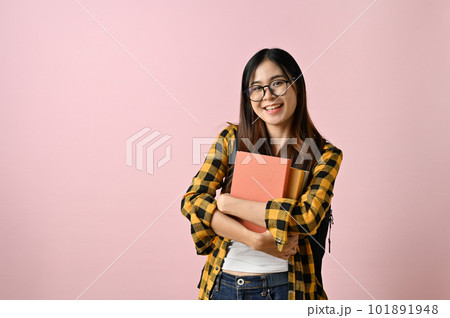 Pretty Asian female college student carrying her schoolbooks, isolated pink background. 101891948