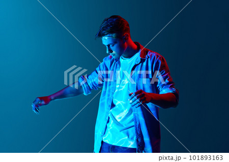 Young man standing with digital neon lights reflection on face and body over blue background. Fantasy and futurism Young man standing with digital neon lights reflection on face and body over blue background. Fantasy and futurism 101893163
