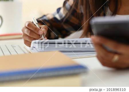 Woman writes hand on agenda while consulting mobile phone on desk at home or in office 101896310