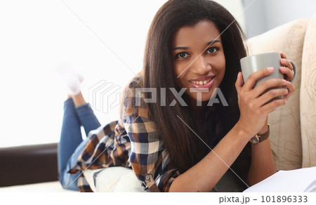 Black woman enjoys relaxing with coffee lying on sofa 101896333