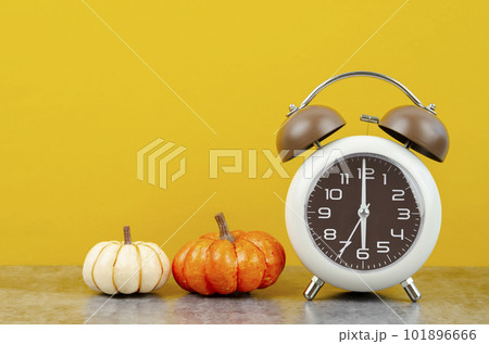 The Vintage alarm clock with autumn pumpkins on yellow background. The Vintage alarm clock with autumn pumpkins on yellow background. 101896666