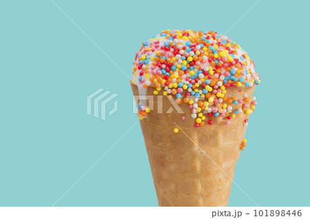 Ice cream cone close up. White ice cream scoop in a waffle cone on a blue background. Sweet dessert decorated with multicolored sprinkles Ice cream cone close up. White ice cream scoop in a waffle cone on a blue background. Sweet dessert decorated with multicolored sprinkles 101898446