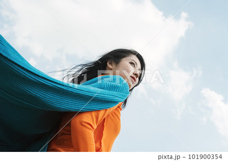 風に吹かれながら青空を見上げる20代の若い女性 風に吹かれながら青空を見上げる20代の若い女性 101900354