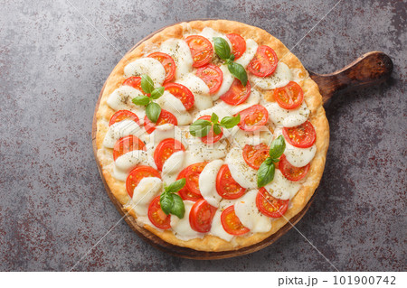 Caprese pizza with melted mozzarella, tomatoes and basil leaves close-up on a wooden board. horizontal top view 101900742