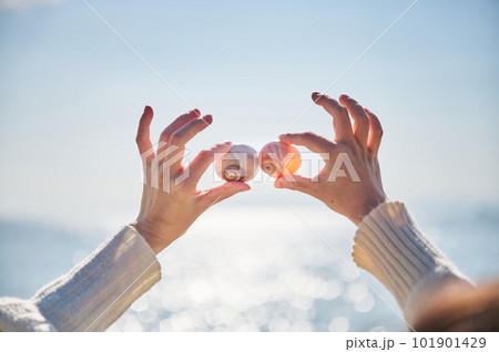 砂浜で拾った貝を高く掲げる若い女性の手 101901429