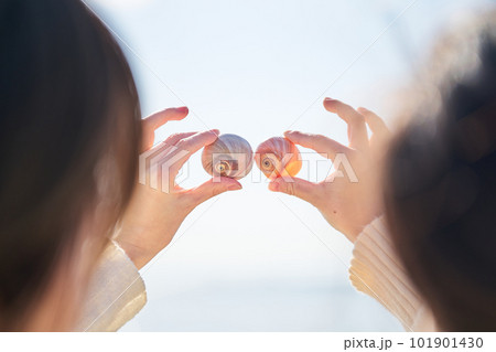 砂浜で拾った貝を高く掲げる若い女性の手 101901430