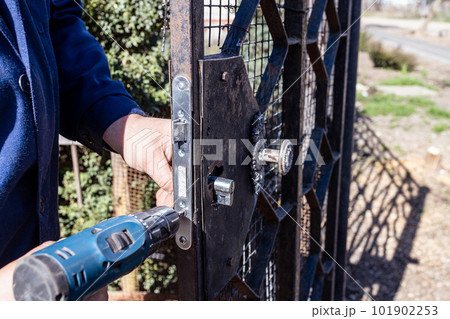 worker fixes of door lock in gate with screwdriver 101902253