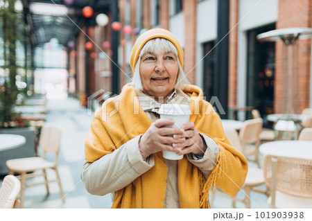 Portrait of old Woman in yellow hat holding cup of hot drink in hand. Attractive female drinking a coffee in paper bio white cup. Drinking take away tea. Breakfast on the go. Portrait of old Woman in yellow hat holding cup of hot drink in hand. Attractive female drinking a coffee in paper bio white cup. Drinking take away tea. Breakfast on the go. 101903938