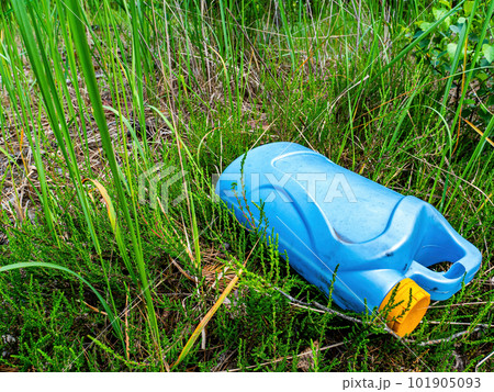 A blue plastic canister in a junkyard in the green grass. 101905093