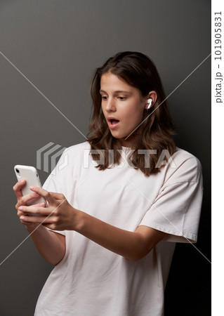 Surprised teen female in earbuds and looking at smartphone in hands 101905831