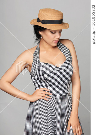 Pensive mixed race woman in chequered summer dress and canotier straw hat 101905832