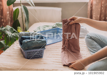Lady folds a t-shirt after washing while sitting on the bed 101905902