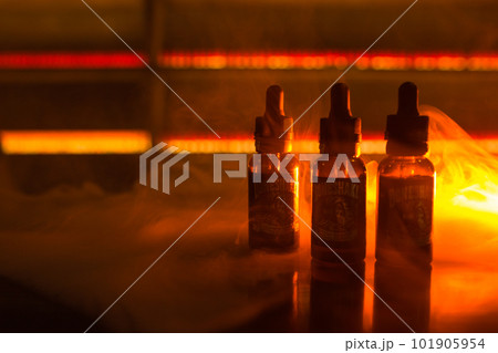 Bubbles liquid bottles on a dark background with smoke and orange light. vape background. Bubbles liquid bottles on a dark background with smoke and orange light. vape background. 101905954