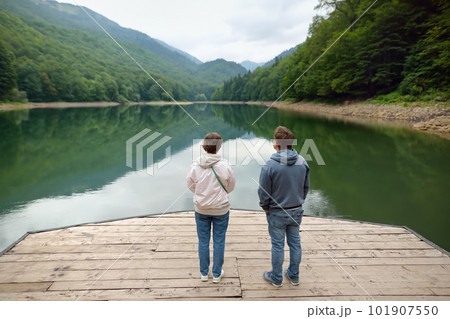 Tourists admiring of breathtaking landscape of mountain lake Biogradsko in alps of Montenegro on spring day. Stunning view of mountains and valleys in national park Biogradska Gora. Tourists admiring of breathtaking landscape of mountain lake Biogradsko in alps of Montenegro on spring day. Stunning view of mountains and valleys in national park Biogradska Gora. 101907550