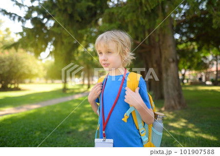 Elementary student boy with backpack, bottle of water and name badge on his neck goes to school. Happy child is waiting of school bus. Elementary student boy with backpack, bottle of water and name badge on his neck goes to school. Happy child is waiting of school bus. 101907588