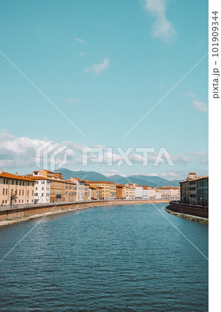 A beautiful view of buildings along the Arno river in Pisa, Italy. A bridge passes over the river and houses on both sides are overlooking the water 101909344