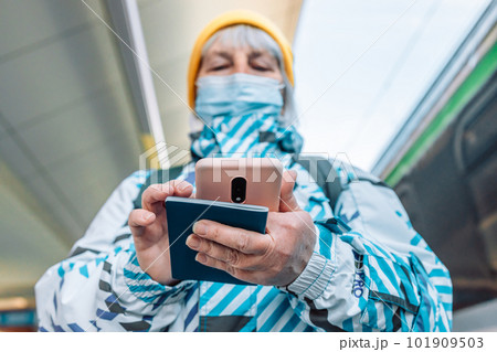 60s woman in face mask waiting on a train station platform with passport and tickets  101909503