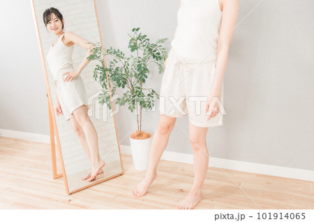 ダイエット・減量に成功して鏡で体型・ボディーラインをチェックするスリムな笑顔の女性 101914065