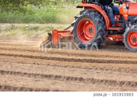 Tractor cultivating land with a rotary tiller in farm. Tractor cultivating land with a rotary tiller in farm. 101915803