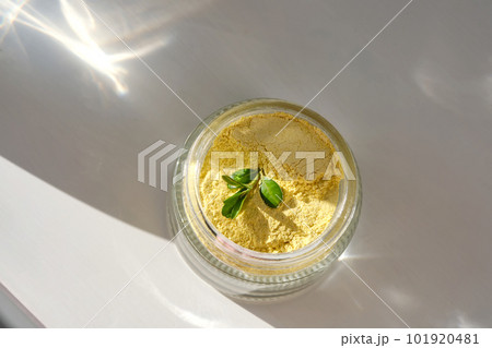 An open jar of a yellow turmeric facial scrub showing off its texture. 101920481