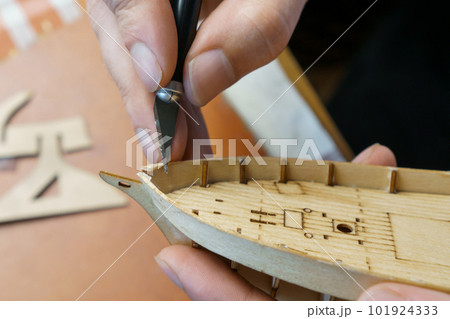 Hands man cutting out details for ship model with clerical knife from plywood. Process of building toy ship, handicraft. 101924333