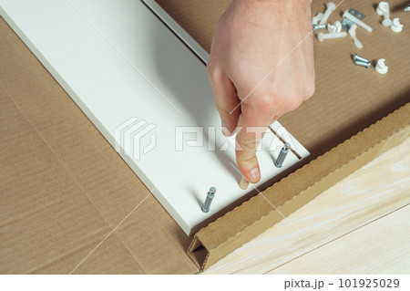 Male hands finger wooden dowel to fix walls of white drawer, assembling dresser or wardrobe. Eccentric furniture ties Male hands finger wooden dowel to fix walls of white drawer, assembling dresser or wardrobe. Eccentric furniture ties 101925029