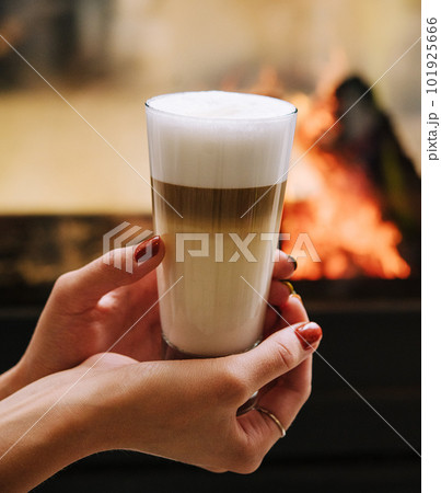 A female hand holding a cup of coffee against fireplace A female hand holding a cup of coffee against fireplace 101925666
